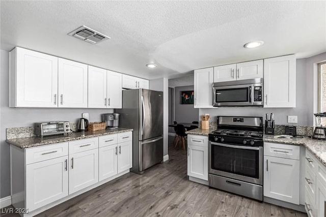 3158 Brockington Dr, Las Vegas, NV 89120 - kitchen with stainless steel appliances, white cabinetry, a textured ceiling, wood finished floors, and light stone countertops