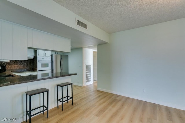 3785 Decade St, Las Vegas, NV 89121 - kitchen featuring freestanding refrigerator, light wood-style floors, a breakfast bar, a peninsula, and white cabinets
