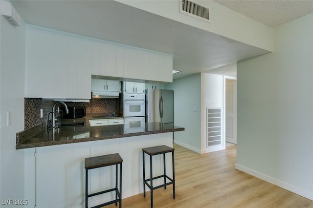 3785 Decade St, Las Vegas, NV 89121 - kitchen featuring freestanding refrigerator, under cabinet range hood, a peninsula, light wood-style floors, and white cabinetry