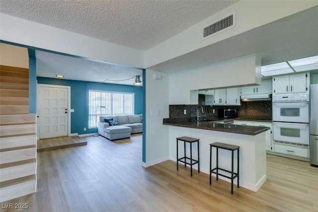 3785 Decade St, Las Vegas, NV 89121 - kitchen featuring double oven, under cabinet range hood, a peninsula, a textured ceiling, and light wood-style flooring