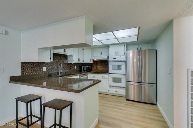 3785 Decade St, Las Vegas, NV 89121 - kitchen featuring stainless steel appliances, under cabinet range hood, a peninsula, decorative backsplash, and light wood-style floors