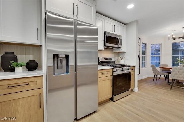 7701 Sea Cliff Way, Las Vegas, NV 89128 - kitchen with appliances with stainless steel finishes, light wood finished floors, a chandelier, light countertops, and decorative backsplash