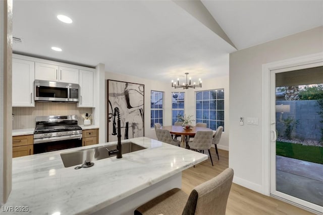 7701 Sea Cliff Way, Las Vegas, NV 89128 - kitchen with appliances with stainless steel finishes, light wood-type flooring, a chandelier, white cabinetry, and decorative backsplash