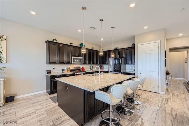 800 Rosewater Dr, Henderson, NV 89011 - kitchen with stainless steel appliances, light stone counters, a kitchen island with sink, a breakfast bar area, and decorative light fixtures