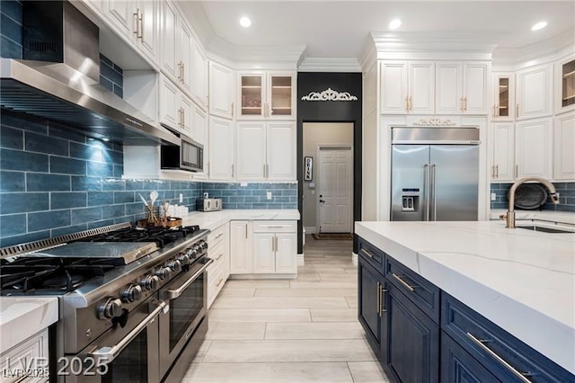 764 Ricota Ct, Henderson, NV 89012 - kitchen featuring high quality appliances, wall chimney exhaust hood, white cabinetry, blue cabinetry, and crown molding