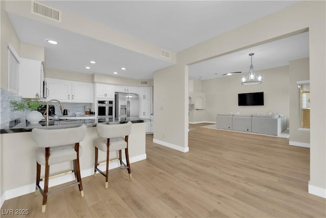 7837 Sea Rock Rd, Las Vegas, NV 89128 - kitchen featuring stainless steel appliances, a peninsula, white cabinets, a kitchen breakfast bar, and open floor plan