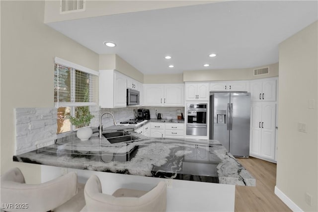 7837 Sea Rock Rd, Las Vegas, NV 89128 - kitchen featuring appliances with stainless steel finishes, a warming drawer, a peninsula, light stone counters, and light wood finished floors