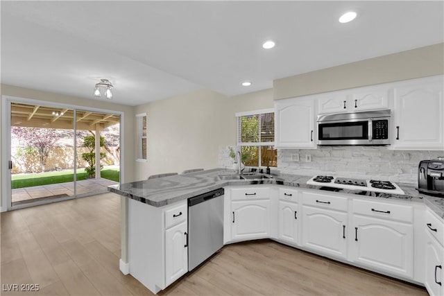 7837 Sea Rock Rd, Las Vegas, NV 89128 - kitchen with stainless steel appliances, a peninsula, backsplash, light stone countertops, and light wood-style floors