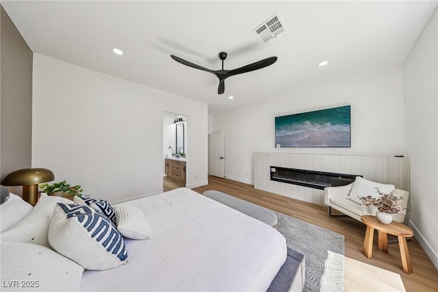 2297 Aria Dr, Henderson, NV 89052 - bedroom with wood finished floors, recessed lighting, ceiling fan, a glass covered fireplace, and ensuite bath