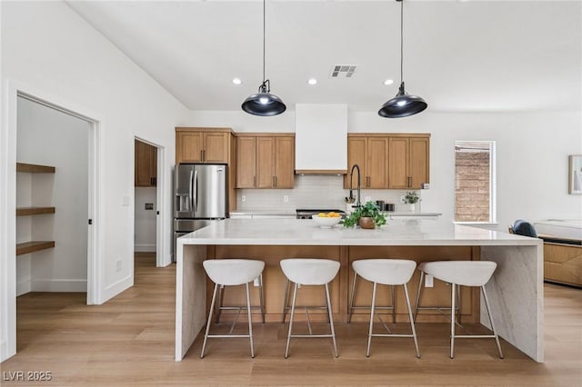 2297 Aria Dr, Henderson, NV 89052 - kitchen with stainless steel fridge with ice dispenser, tasteful backsplash, light countertops, light wood-type flooring, and a spacious island