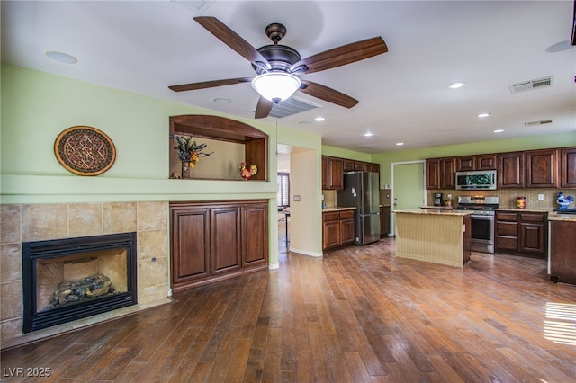 9022 Sosa Creek Ave, Las Vegas, NV 89149 - kitchen with stainless steel appliances, a kitchen island, dark wood-style floors, a ceiling fan, and a fireplace