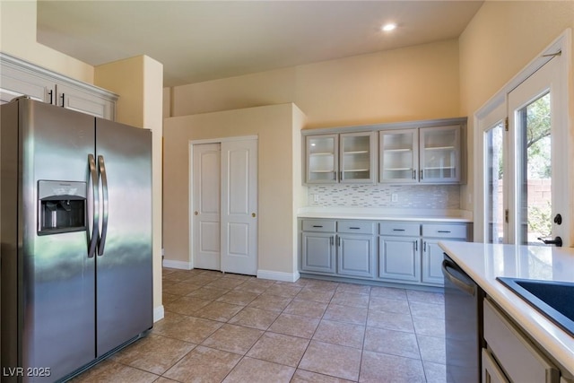 6740 Arctic Breeze St, North Las Vegas, NV 89084 - kitchen featuring appliances with stainless steel finishes, light countertops, glass insert cabinets, decorative backsplash, and light tile patterned floors