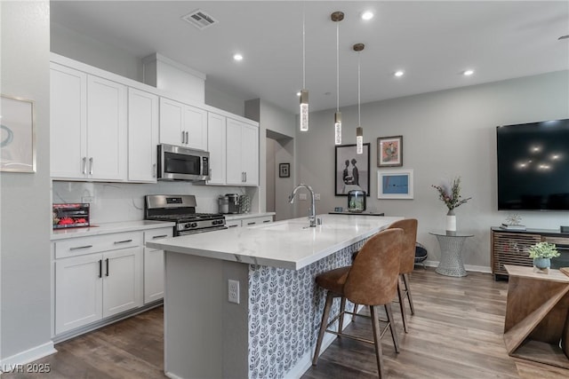 2530 Catallo St, Henderson, NV 89044 - kitchen with stainless steel appliances, dark wood-style floors, a kitchen island with sink, a breakfast bar area, and decorative light fixtures