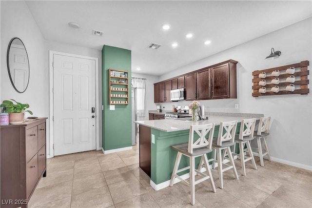 4332 Stardusk Falls Ave, North Las Vegas, NV 89084 - kitchen featuring stainless steel microwave, stove, light countertops, a breakfast bar, and dark brown cabinets