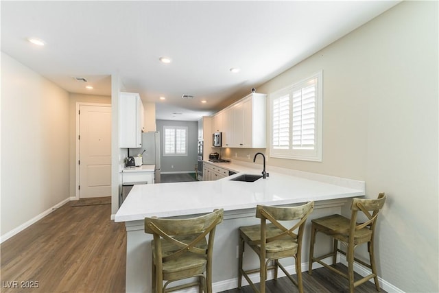 10711 Silver Pond Ave, Las Vegas, NV 89135 - kitchen with white cabinets, a peninsula, a kitchen breakfast bar, light countertops, and dark wood-style flooring