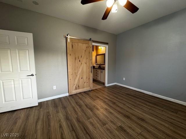 2704 Willow Wren Dr, North Las Vegas, NV 89084 - unfurnished bedroom with dark wood-style flooring, a barn door, a ceiling fan, and ensuite bath