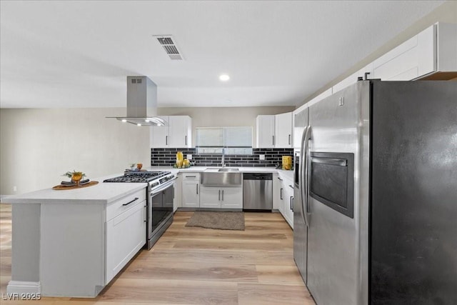 321 Oil Lantern Ln, Las Vegas, NV 89145 - kitchen featuring stainless steel appliances, island exhaust hood, white cabinets, light wood finished floors, and decorative backsplash