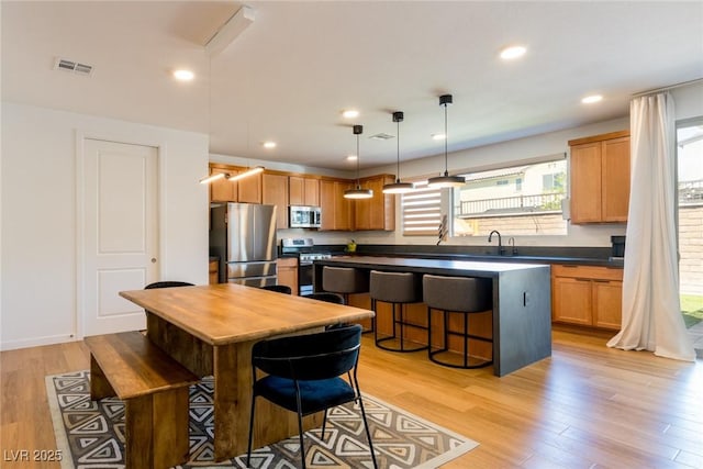 6927 Desert Finch St, North Las Vegas, NV 89084 - kitchen with stainless steel appliances, dark countertops, a breakfast bar area, light wood-style flooring, and decorative light fixtures