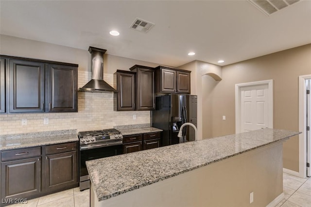 11063 Mount George St, Las Vegas, NV 89179 - kitchen with gas range, black refrigerator with ice dispenser, wall chimney range hood, light stone countertops, and light tile patterned flooring