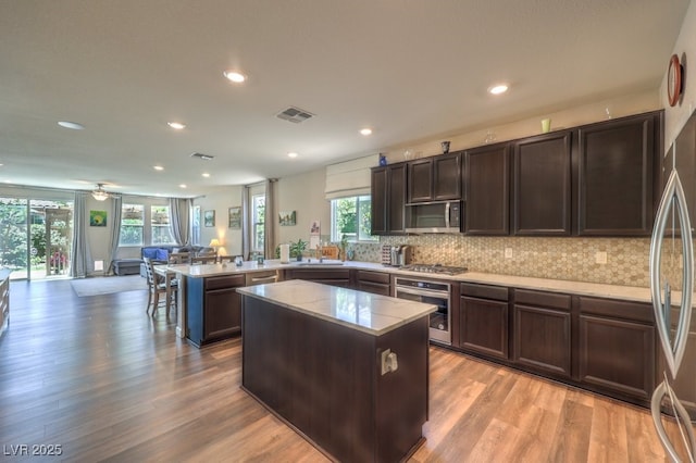 9785 W Meranto Ave, Las Vegas, NV 89178 - kitchen featuring appliances with stainless steel finishes, a peninsula, light wood-style flooring, tasteful backsplash, and a kitchen island