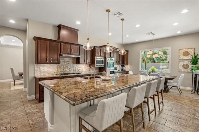 9747 Cathedral Pines Ave, Las Vegas, NV 89149 - kitchen with arched walkways, tasteful backsplash, appliances with stainless steel finishes, a kitchen island with sink, and recessed lighting