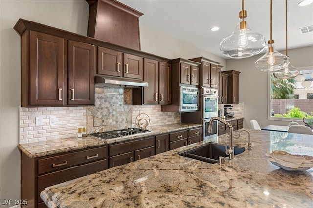9747 Cathedral Pines Ave, Las Vegas, NV 89149 - kitchen with under cabinet range hood, appliances with stainless steel finishes, tasteful backsplash, light stone countertops, and dark brown cabinetry