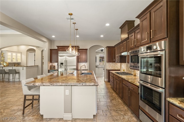 9747 Cathedral Pines Ave, Las Vegas, NV 89149 - kitchen with built in appliances, a kitchen breakfast bar, stone tile flooring, backsplash, and arched walkways