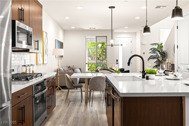 11756 Emerald Lake Ave, Las Vegas, NV 89138 - kitchen featuring appliances with stainless steel finishes, light countertops, light wood-type flooring, hanging light fixtures, and tasteful backsplash