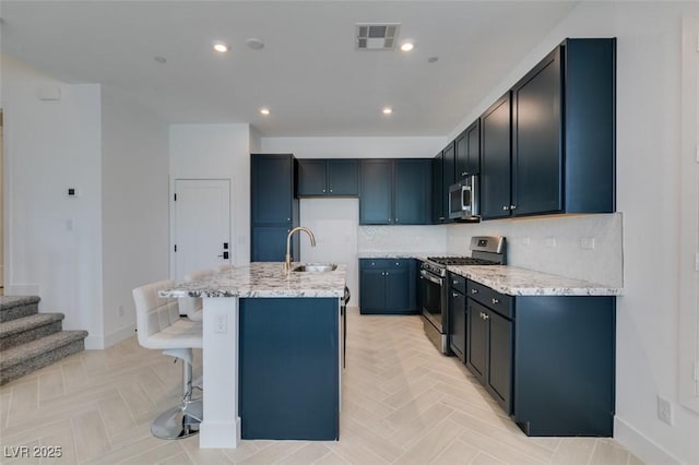 9844 Kings Glen St, Las Vegas, NV 89141 - kitchen with stainless steel appliances, light stone counters, a center island with sink, decorative backsplash, and a kitchen breakfast bar