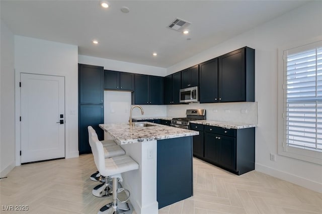9844 Kings Glen St, Las Vegas, NV 89141 - kitchen with stainless steel appliances, light stone counters, a kitchen bar, a kitchen island with sink, and recessed lighting