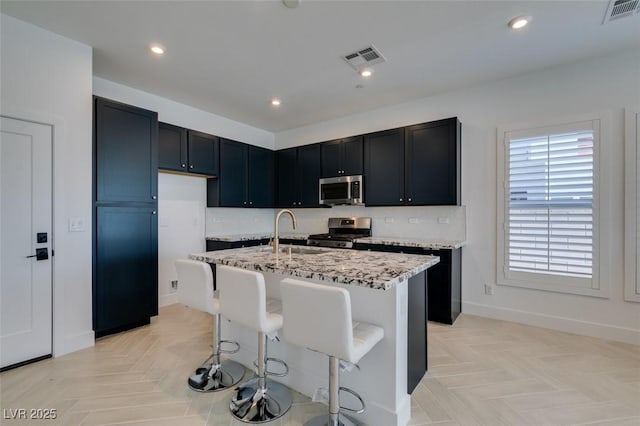 9844 Kings Glen St, Las Vegas, NV 89141 - kitchen with appliances with stainless steel finishes, light stone counters, a kitchen island with sink, recessed lighting, and a breakfast bar