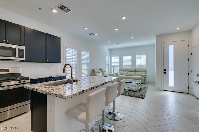 9844 Kings Glen St, Las Vegas, NV 89141 - kitchen with appliances with stainless steel finishes, a center island with sink, light stone countertops, a breakfast bar, and open floor plan