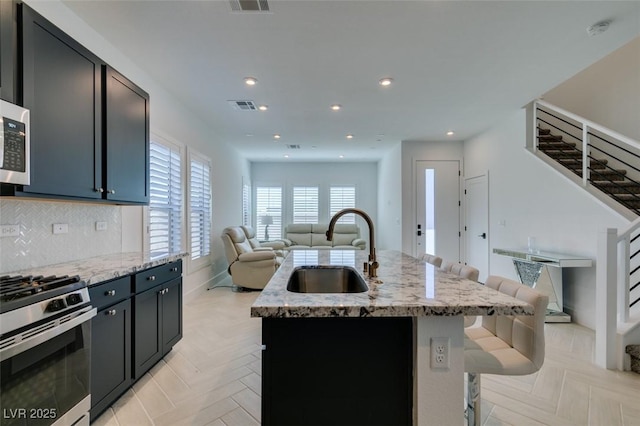 9844 Kings Glen St, Las Vegas, NV 89141 - kitchen featuring open floor plan, stainless steel range with gas cooktop, light stone counters, an island with sink, and decorative backsplash