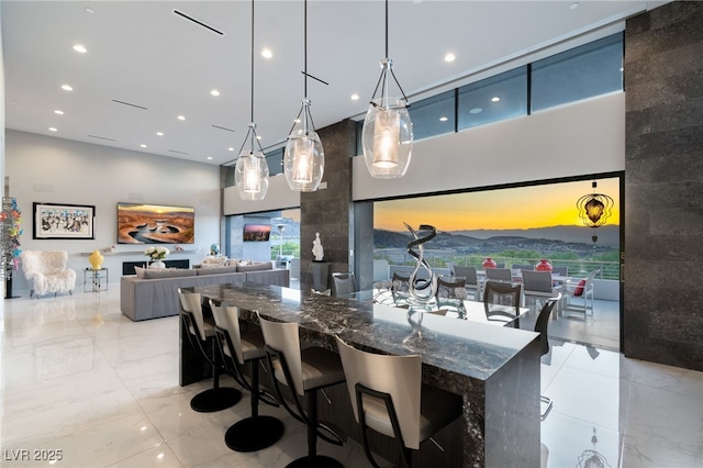 671 Scenic Rim Dr, Henderson, NV 89012 - kitchen featuring a towering ceiling, light marble finish floors, recessed lighting, dark stone countertops, and decorative light fixtures