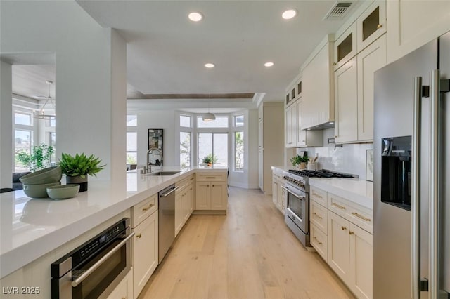 9425 Villa Ridge Dr, Las Vegas, NV 89134 - kitchen featuring stainless steel appliances, recessed lighting, light countertops, light wood-style flooring, and glass insert cabinets