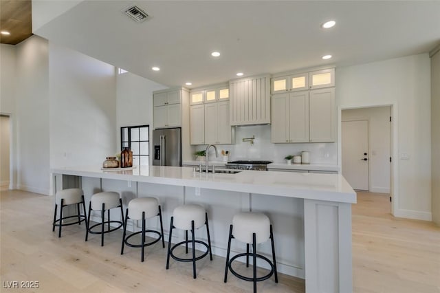 9520 Sundial Dr, Las Vegas, NV 89134 - kitchen with stainless steel refrigerator with ice dispenser, light wood-type flooring, a large island with sink, a breakfast bar, and light countertops