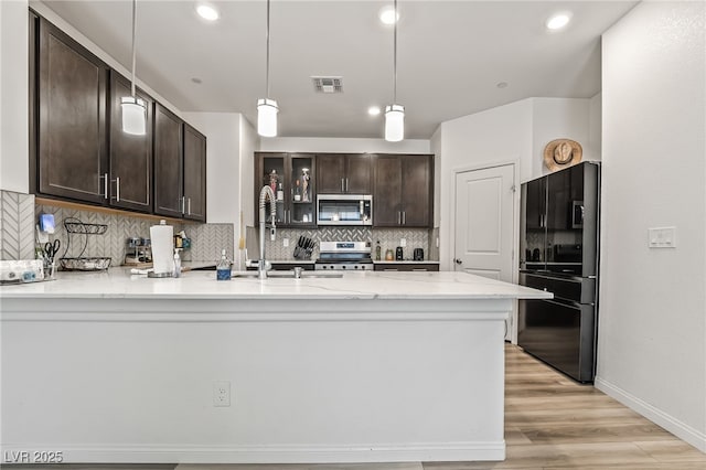 3641 Portici Ln, Henderson, NV 89044 - kitchen with stainless steel appliances, a peninsula, dark brown cabinetry, tasteful backsplash, and light wood-type flooring