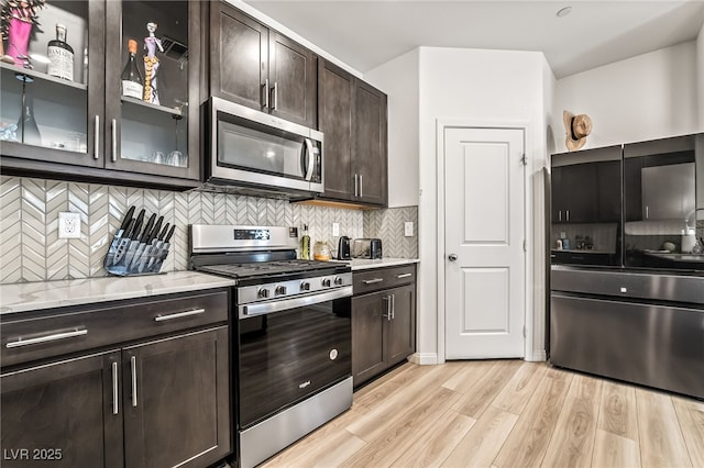 3641 Portici Ln, Henderson, NV 89044 - kitchen featuring appliances with stainless steel finishes, dark brown cabinets, light wood-style floors, tasteful backsplash, and glass insert cabinets