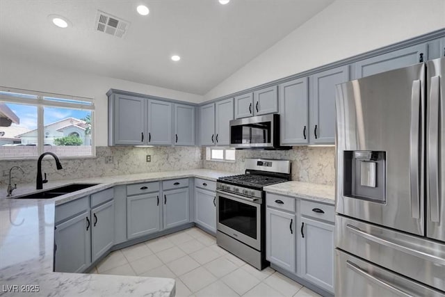 1613 Glenrosa Dr, North Las Vegas, NV 89031 - kitchen featuring appliances with stainless steel finishes, gray cabinets, vaulted ceiling, light stone counters, and tasteful backsplash