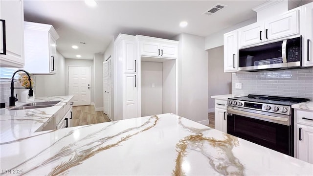 744 Hubbard St, Las Vegas, NV 89110 - kitchen with stainless steel appliances, tasteful backsplash, white cabinetry, light wood-style floors, and light stone countertops