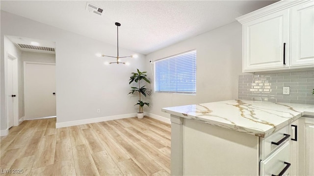 744 Hubbard St, Las Vegas, NV 89110 - kitchen with light wood finished floors, backsplash, light stone countertops, white cabinetry, and decorative light fixtures