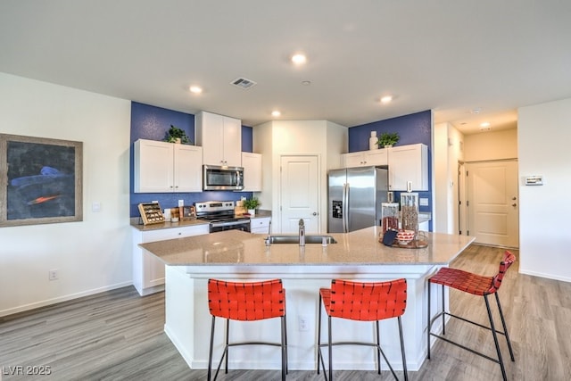7965 Aurora Sky St Unit 623, North Las Vegas, NV 89084 - kitchen featuring stainless steel appliances, light wood-type flooring, white cabinetry, a kitchen island with sink, and light stone countertops