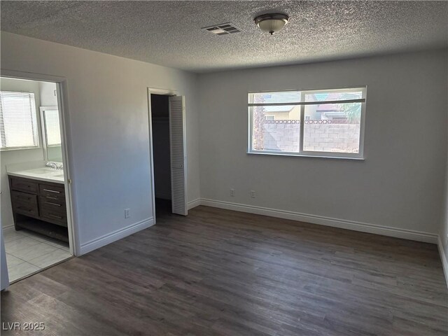 6402 Agua Dr, Las Vegas, NV 89103 - unfurnished bedroom with multiple windows, wood finished floors, a closet, a textured ceiling, and connected bathroom