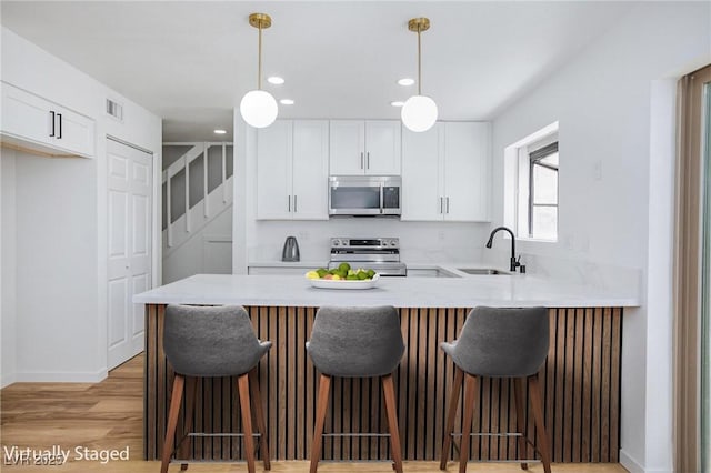 572 Tam O Shanter, Las Vegas, NV 89109 - kitchen with appliances with stainless steel finishes, a peninsula, white cabinetry, light wood-style floors, and pendant lighting