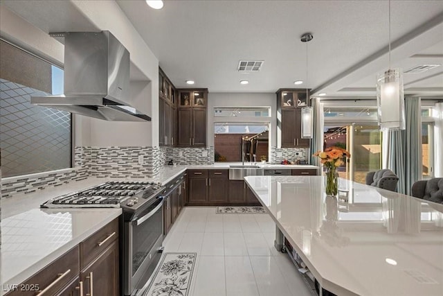 6618 Tangled Vines Ave, Las Vegas, NV 89139 - kitchen with gas stove, island range hood, dark brown cabinetry, light tile patterned floors, and decorative backsplash