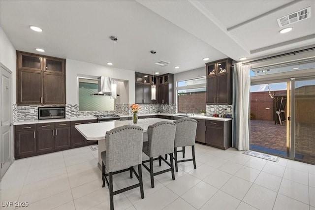 6618 Tangled Vines Ave, Las Vegas, NV 89139 - kitchen with appliances with stainless steel finishes, wall chimney exhaust hood, backsplash, a breakfast bar, and dark brown cabinetry