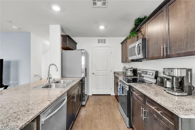 6953 Midnight Bronze St, North Las Vegas, NV 89086 - kitchen with appliances with stainless steel finishes, dark brown cabinets, light wood finished floors, light stone countertops, and recessed lighting