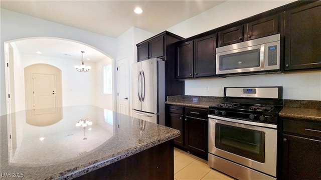 145 Forest Crossing Ct, Las Vegas, NV 89148 - kitchen with stainless steel appliances, arched walkways, dark stone countertops, a chandelier, and light tile patterned floors