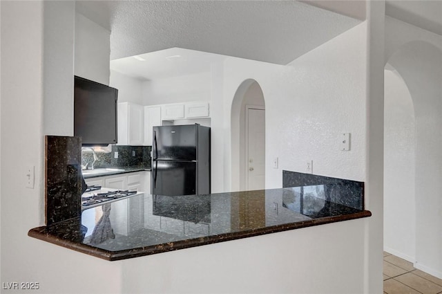 900 Heavenly Hills Ct Unit 114, Las Vegas, NV 89145 - kitchen with freestanding refrigerator, a peninsula, dark stone countertops, white cabinetry, and a textured ceiling