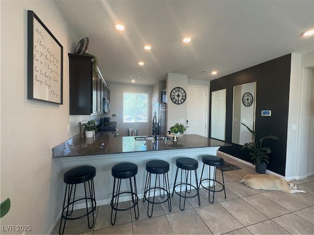 7636 Bandon Cliffs St, North Las Vegas, NV 89084 - kitchen featuring a peninsula, freestanding refrigerator, a breakfast bar area, dark stone counters, and recessed lighting
